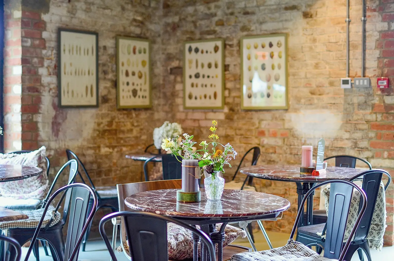 Marble café tables with jugs of flowers against an old brick wall hung with framed prints